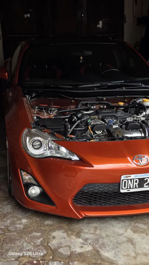El Toyota 86 naranja en el patio, sin capó, con todo el motor a la vista, esperando.