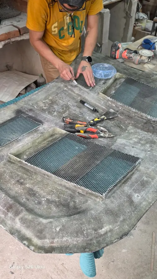 El capó de fibra boca arriba sobre caballetes, con mallas de metal desplegado montadas dentro de cada toma de aire y herramientas alrededor.