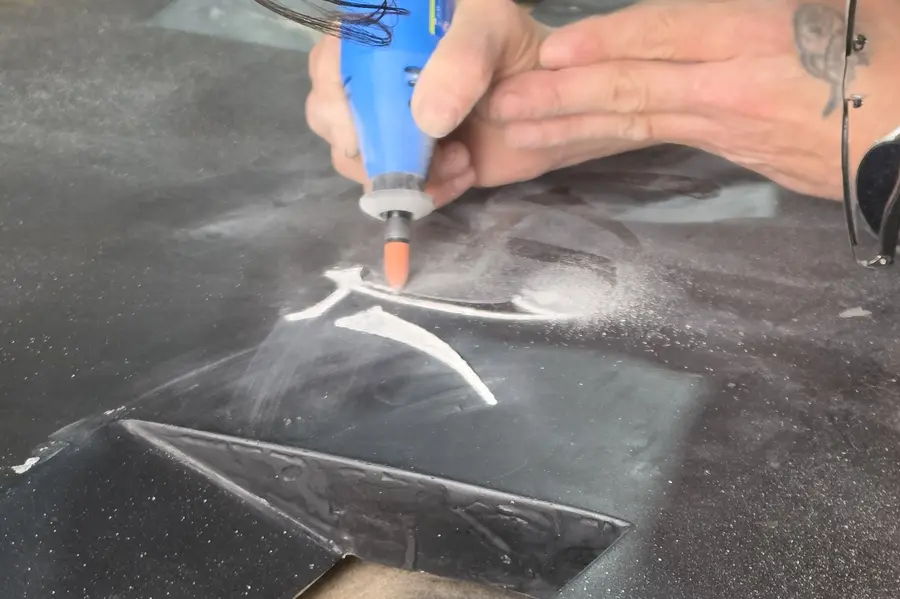 Primer plano de la punta de la herramienta grabando la pintura negra, con el polvo blanco saltando alrededor del trazo.