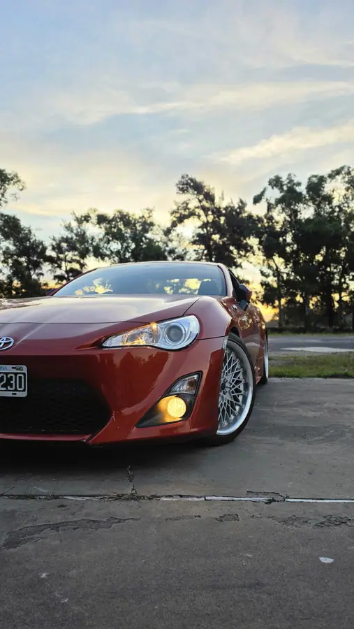 El frente del Toyota 86 naranja al atardecer, con los faros antiniebla amarillos encendidos.