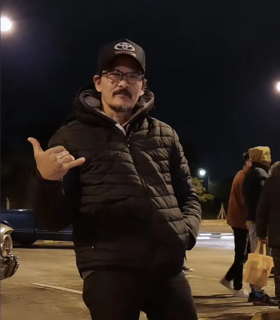 Pedro Ariel Maciel, de noche, con gorra de Toyota y campera negra, haciendo un gesto con la mano a la cámara.